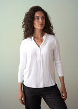 Woman wearing a long sleeve white top with button detail styled with dark blue trousers
