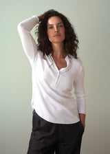Woman wearing a long sleeve white top with button detail with hand tucked into pocket of dark blue jeans