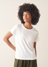 Woman wearing white, round neck t-shirt and dark green wide leg trousers against a plain background