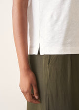 Woman wearing white, round neck t-shirt and dark green wide leg trousers against a plain background