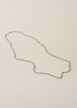 An ultra-long, fine gold chain necklace adorned with twinkling silver beads, on a beige background