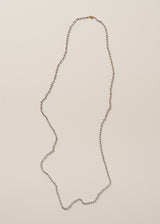 An ultra-long, fine gold chain necklace adorned with twinkling silver beads, on a beige background