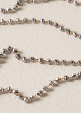 Close up of an ultra-long, fine gold chain necklace adorned with twinkling silver beads on beige background