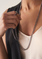 Women wearing an ultra-long twinkling navy blue beaded necklace with a fine gold chain, over a satin top