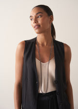 Women wearing an ultra-long twinkling navy blue beaded necklace with a fine gold chain, styled with a satin top, black satin waistcoat, and trousers