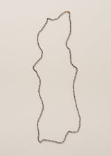 An ultra-long twinkling navy blue beaded necklace with a fine gold chain, on a beige background