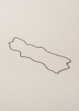 An ultra-long twinkling navy blue beaded necklace with a fine gold chain, on a beige background