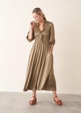 A woman wearing a light khaki green olive satin midi dress with smocked detail and ruffle collar