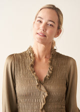 A woman wearing a light khaki green olive satin midi dress with smocked detail and ruffle collar