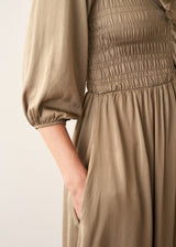 A woman wearing a light khaki green olive satin midi dress with smocked detail and ruffle collar
