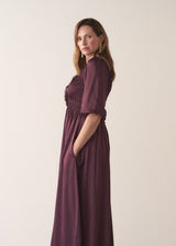Woman wearing a plum sati midi dress standing against a plain background