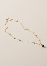 Long golden chain necklace with gold beads and a black pendant on a beige background
