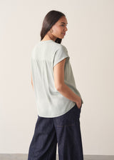Woman wearing light green blouse and denim jeans against a plain background.