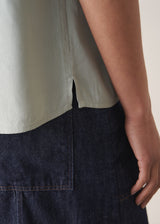 Woman wearing light green blouse and denim jeans against a plain background.