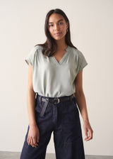 Woman wearing light green blouse and denim jeans against a plain background.