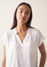 Woman wearing a white blouse and denim cullottes against a plain background