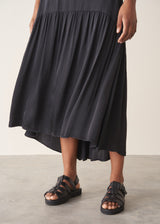 Woman wearing a white top and black satin tiered midi skirt against a plain background