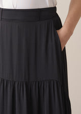 Close up of woman wearing a black satin tiered midi skirt with hand highlighting pocket detail