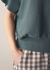 Woman wearing a teal v-neck sweater and checked barrel leg trousers