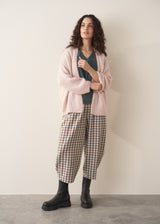 Woman wearing a teal v-neck sweater and checked barrel leg trousers paired with a blush pink cardigan and chunky boots