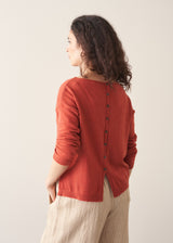 Woman wearing a red cashmere sweater and beige linen trousers against a plain background