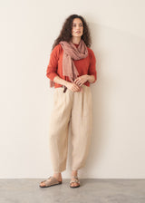 Woman wearing a red cashmere sweater and beige linen trousers against a plain background