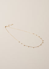 Delicate gold chain necklace with small bead detailing on beige background