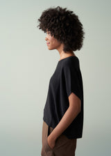 Side view of a woman wearing a black top and khaki trousers against a plain background