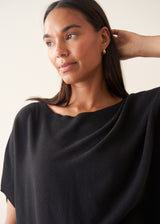 A woman wearing a black short-sleeve boat-neck sweater with black wide-leg trousers.