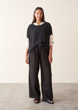 A woman wearing a black short-sleeve boat-neck sweater with black wide-leg trousers.
