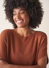 Woman wearing a light brown knitted top with a cream linen maxi skirt.
