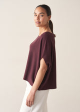 Woman wearing aubergine short sleeve knitted sweater and white barrel leg jeans