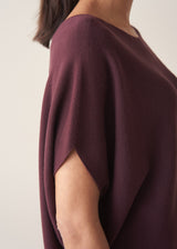 Woman wearing aubergine short sleeve knitted sweater and white barrel leg jeans