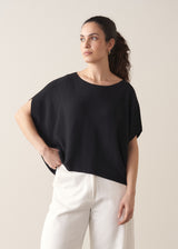 Woman wearing black relaxed sleeve sweater and white barrel leg jeans