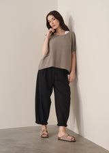 Woman wearing light stone sleeveless knit sweater with black jersey trousers