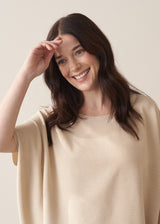 Woman wearing light oatmeal sleeveless sweater and dark green trousers