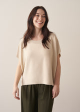 Woman wearing light oatmeal sleeveless sweater and dark green trousers