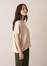 Woman wearing light oatmeal sleeveless sweater and dark green trousers