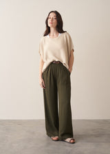 Woman wearing light oatmeal sleeveless sweater and dark green trousers