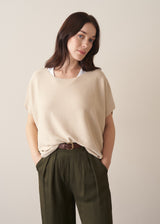 Woman wearing light oatmeal sleeveless sweater and dark green trousers
