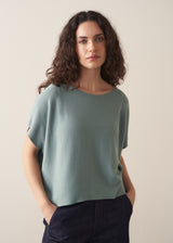 Woman wearing sage short sleeve draped sweater with blue jeans