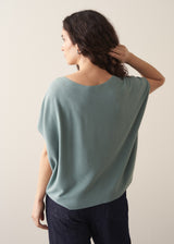 Woman wearing sage short sleeve draped sweater with blue jeans