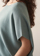 Woman wearing sage short sleeve draped sweater with blue jeans