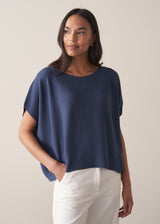 Woman wearing a navy blue sleeveless sweater and white barrel leg jeans