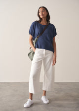 Woman wearing a navy blue sleeveless sweater and white barrel leg jeans and trainers