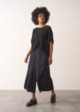 Woman wearing a black sheer sparkle top against a plain background