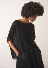 Woman wearing a black sheer sparkle top against a plain background