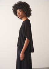 Woman wearing a black sheer sparkle top against a plain background