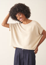 Woman wearing cream light knit sweater and blue denim jeans against a plain background.