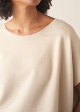 Woman wearing cream light knit sweater and blue denim jeans against a plain background.